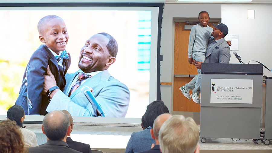 Pro Football Hall of Famer Ray Lewis holds up local youth Blair Pinnacle, re-creating a moment from 2019's groundbreaking ceremony for UMB’s Community Engagement Center