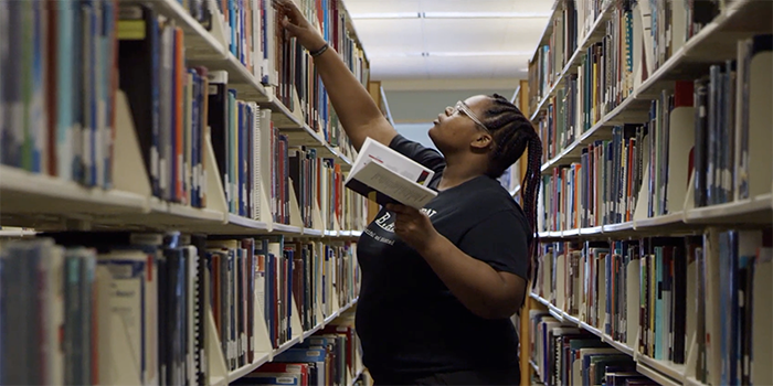 A CURE Scholar selecting books from a library