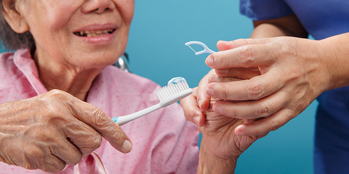 Caregiver assists elderly woman with toothbrush and dental floss stick