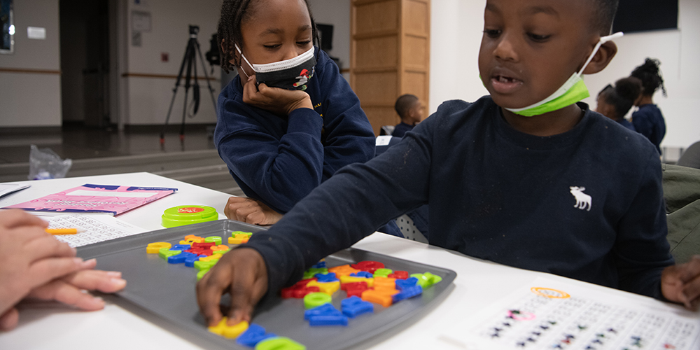 Children arrange colorful letters on a tray