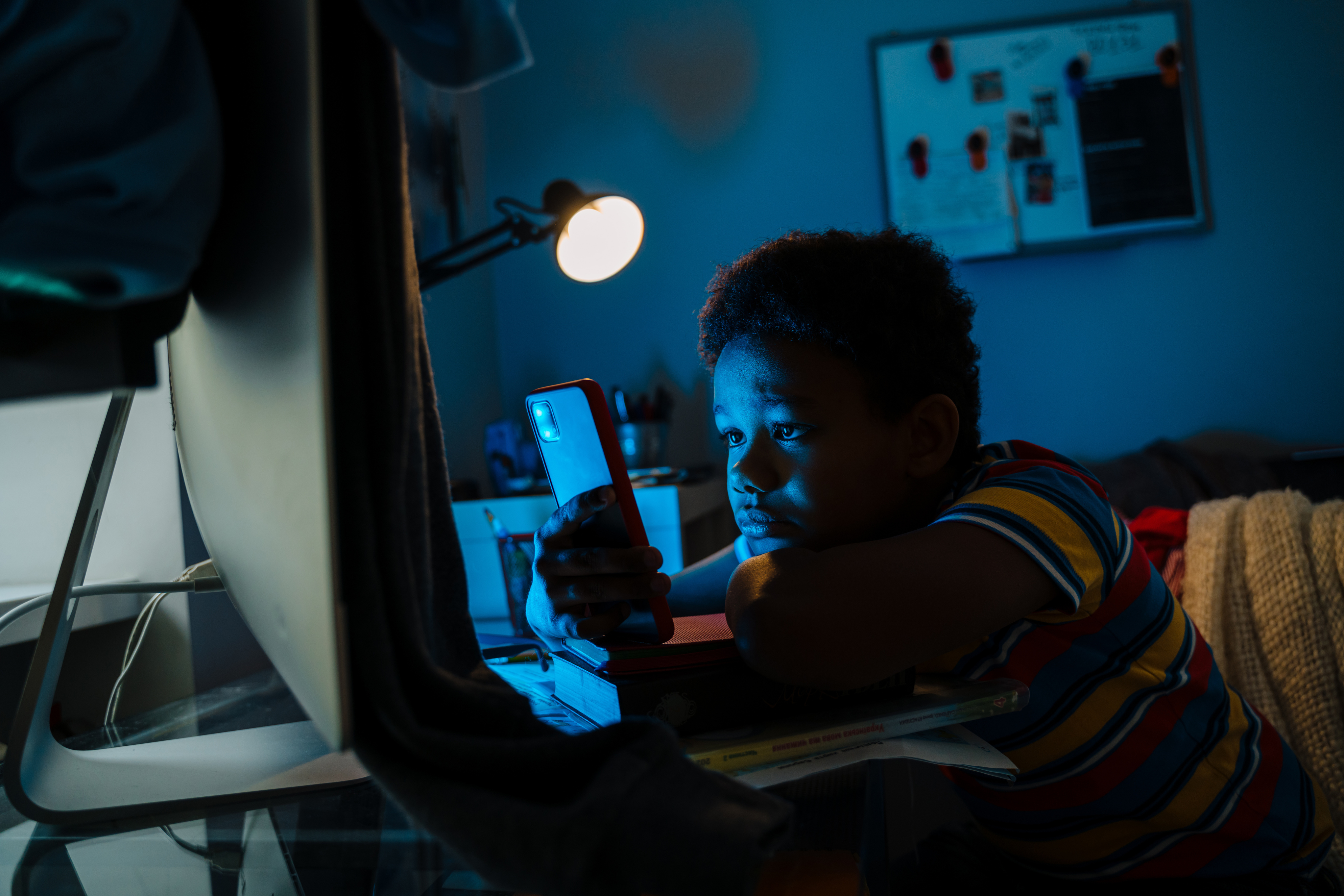 boy using mobile phone while sitting by computer screen