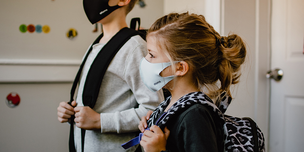 Two kids standing side by side wearing masks