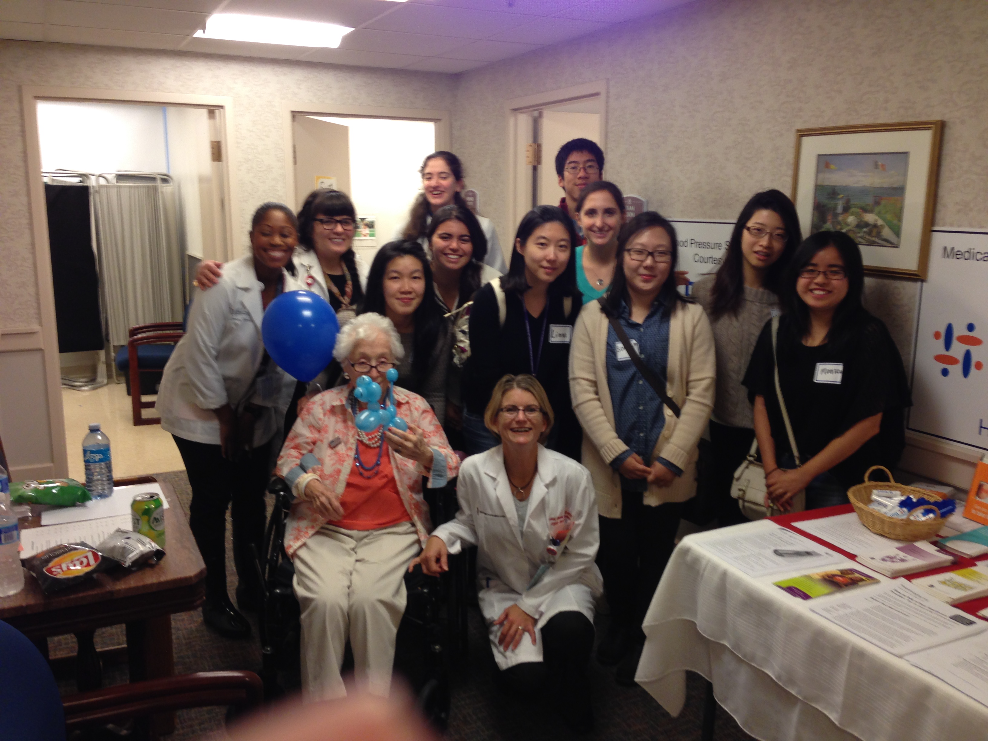 Group of students and physician posing with elderly patient in room