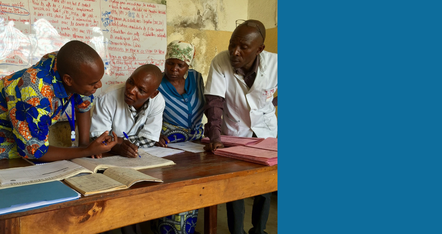 Three people in Africa lean over documents on table with a white board behind them