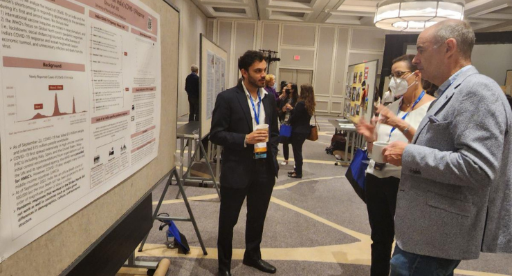 A student stands in front of his poster speaking with two other people