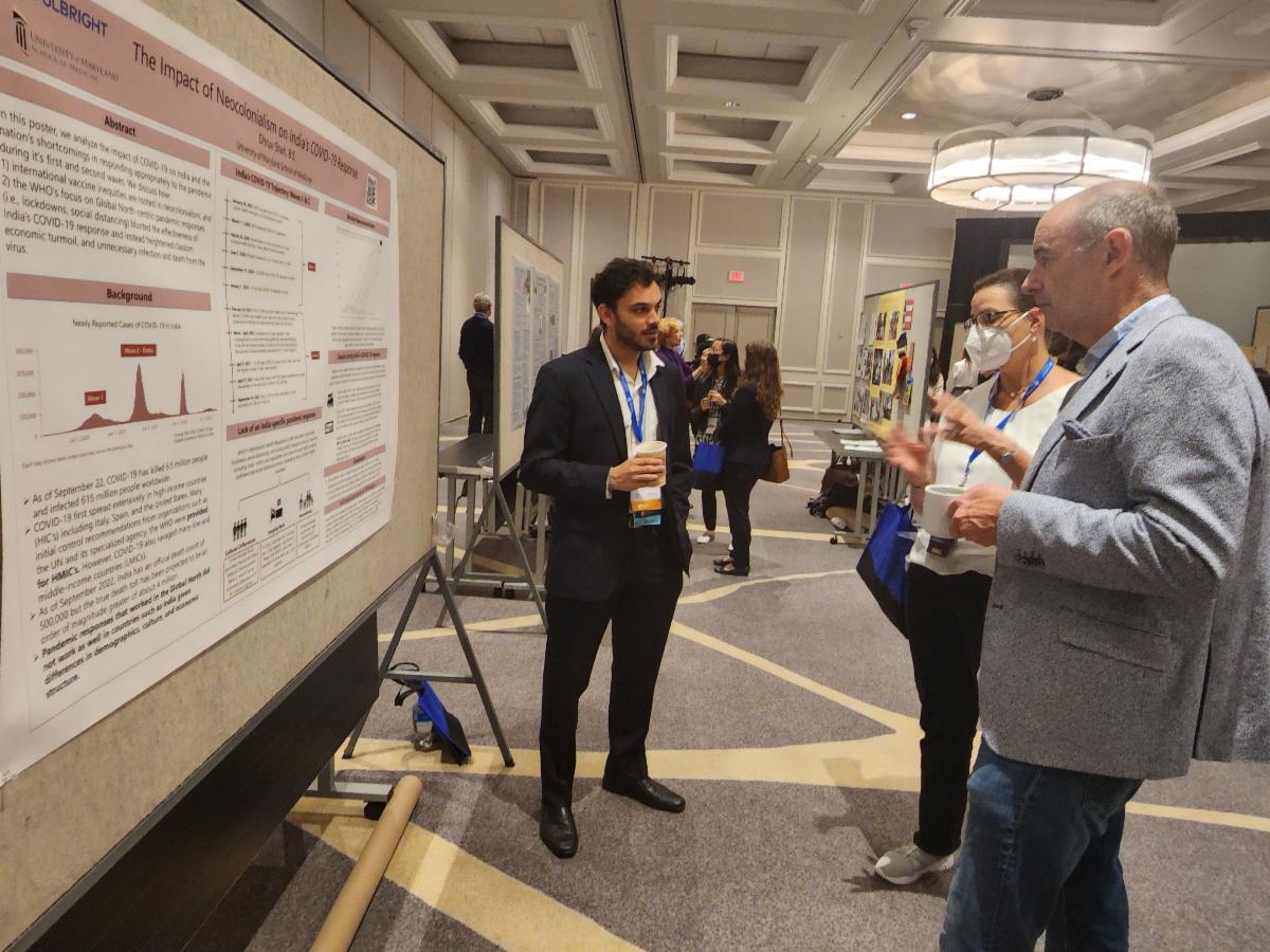 A student stands in front of his poster speaking with two other people