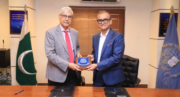 Two men in suits hold a small plaque between them in a conference room.