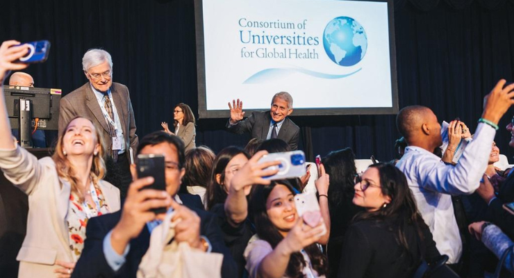 Dr. Anthony poses on a stage with a group of people taking selfies