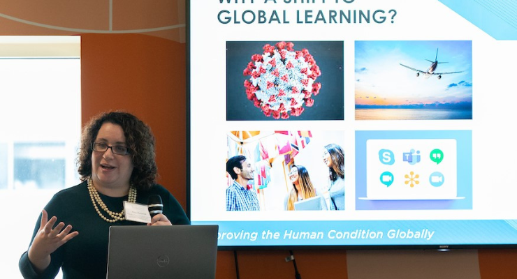 A woman speaks at a podium in front of a PowerPoint presentation on-screen