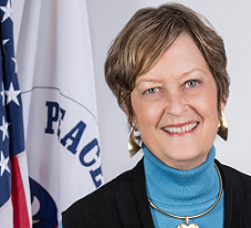 Headshot of a woman in front of a white Peace Corp flag