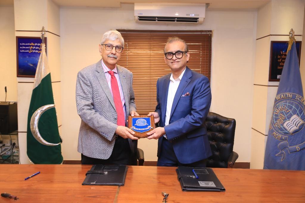 Two men in suits hold a small plaque between them in a conference room.