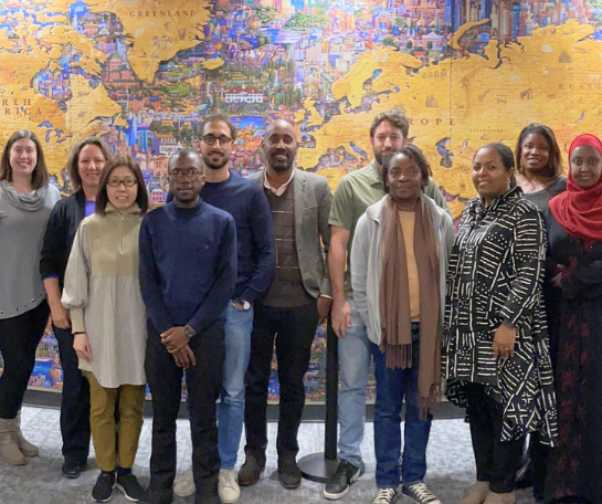 A large group of people pose for a group photo in front of a map.