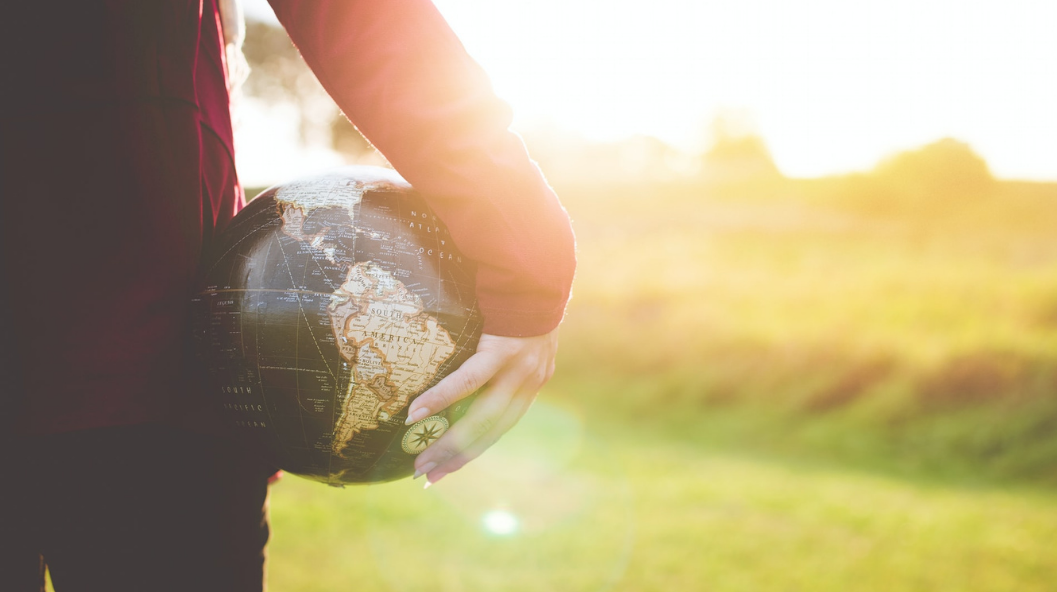 A person's hand holding a globe against their thigh with a sunshiny outdoor background