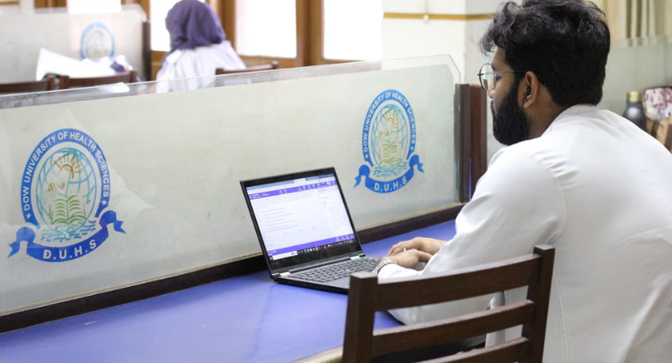 A student in a white lab coat sits in front of a laptop