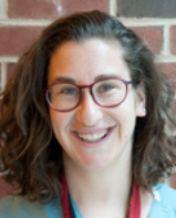 Headshot of a woman wearing glasses in front of a brick wall