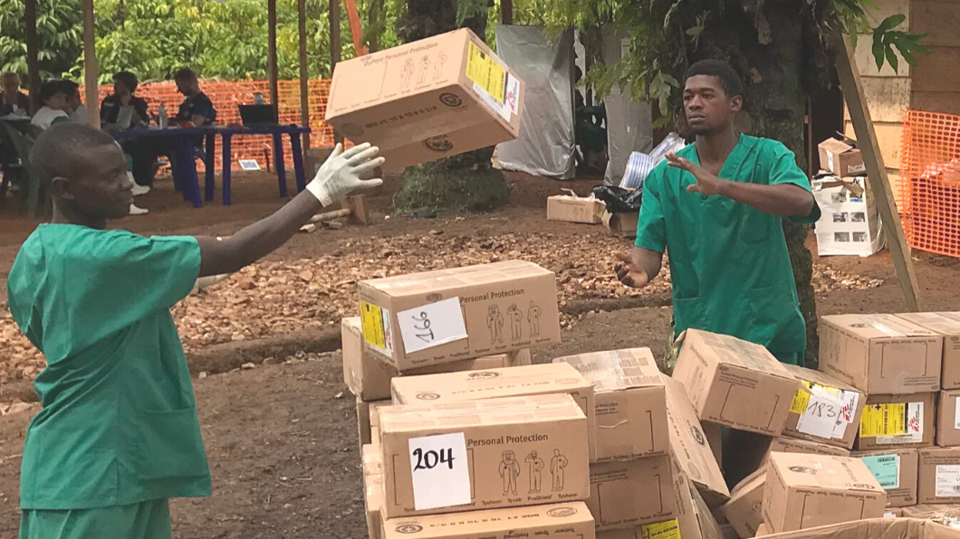 Two men in green scrubs toss brown shopping boxes