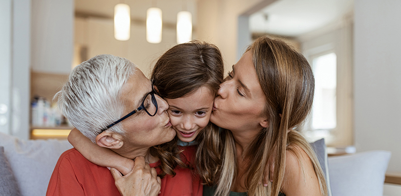 An older woman and younger woman kissing a child's cheeks