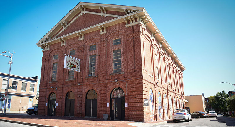 A large brick building with a hanging sign that reads Hollins Market