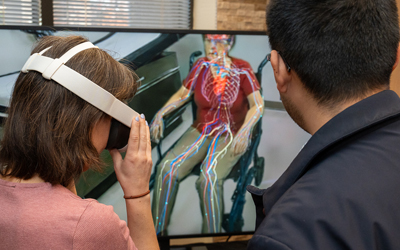 Instructor highlights virtual beating heart for woman wearing virtual reality goggles.