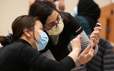 Belinda Tamrakar, a first-year student at the University of Maryland School of Pharmacy (left), learns how to prep the COVID-19 vaccine doses. 