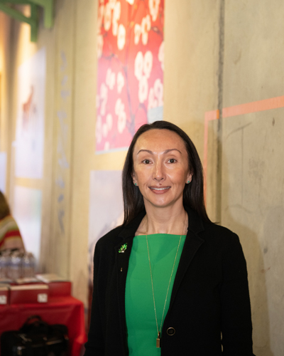 At the Pearl Street Gallery, Oksana Mishler, clinical assistant professor at the University of Maryland School of Dentistry, stands in front of a photo of her acrylic painting “Cherry Blossoms,” which was featured in the second edition of “1807,” UMB's art and literary journal.