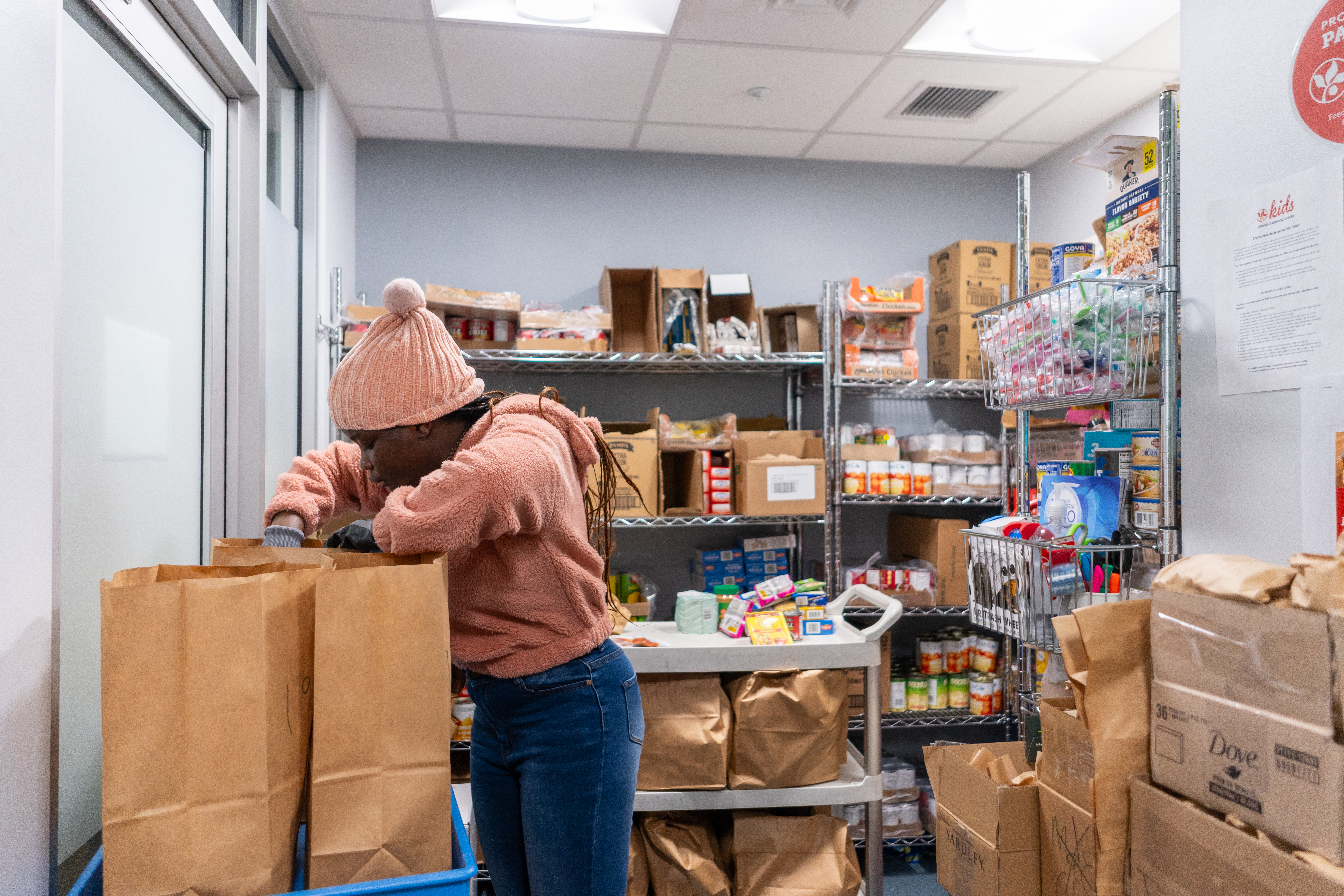 A student stuffing a paper bag with food inside the pantry lined with canned goods