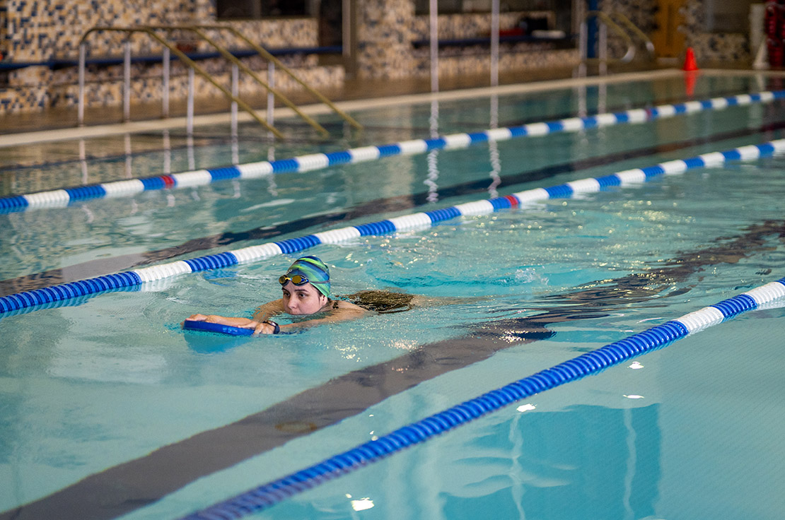 Student in pool swimming with assistant device