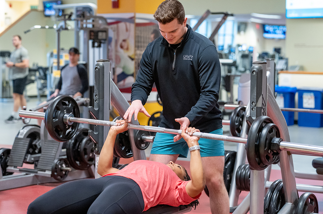 A personal trainer helping a client lift a weight