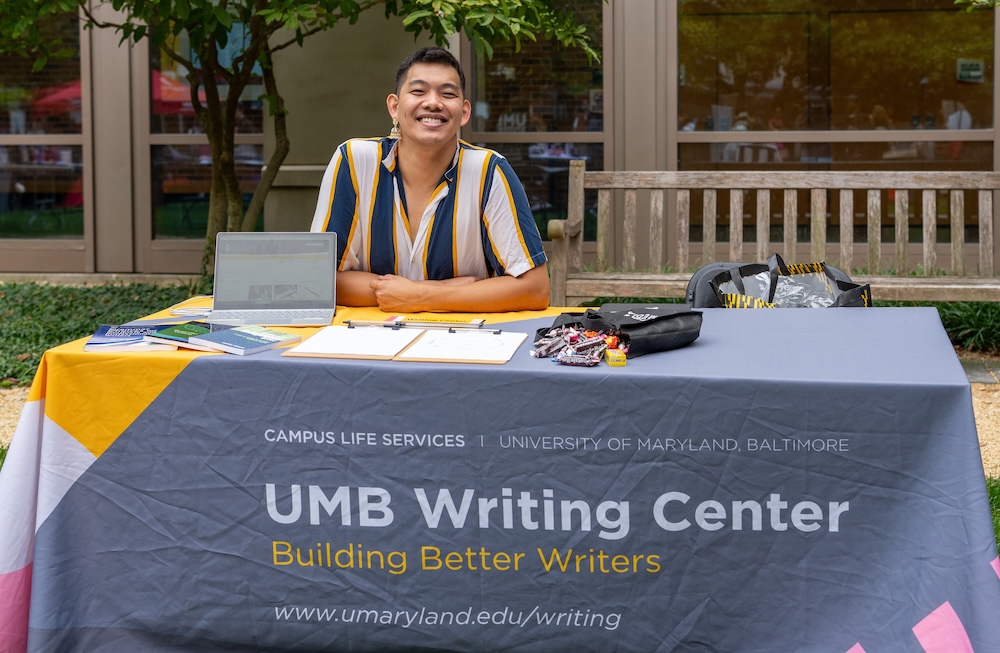 A student sitting behind the Writing Center table at a campus event