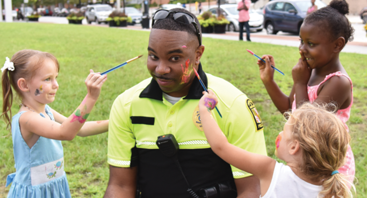 A UMB police officer has his face painted by adolescents.