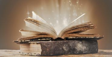 Old books on wooden table. Light is spewing out of the open book.